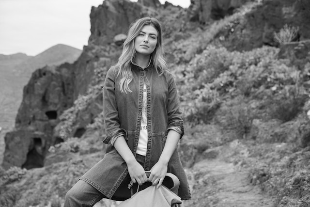 Stehende Frau mit langer Denim Jeansjacke und Handtasche